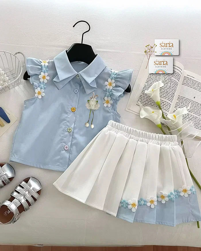 Light blue blouse with floral embroidery and white pleated skirt on a white surface.