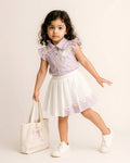 Young girl in a light purple shirt and white skirt with floral patterns, holding a white bag.